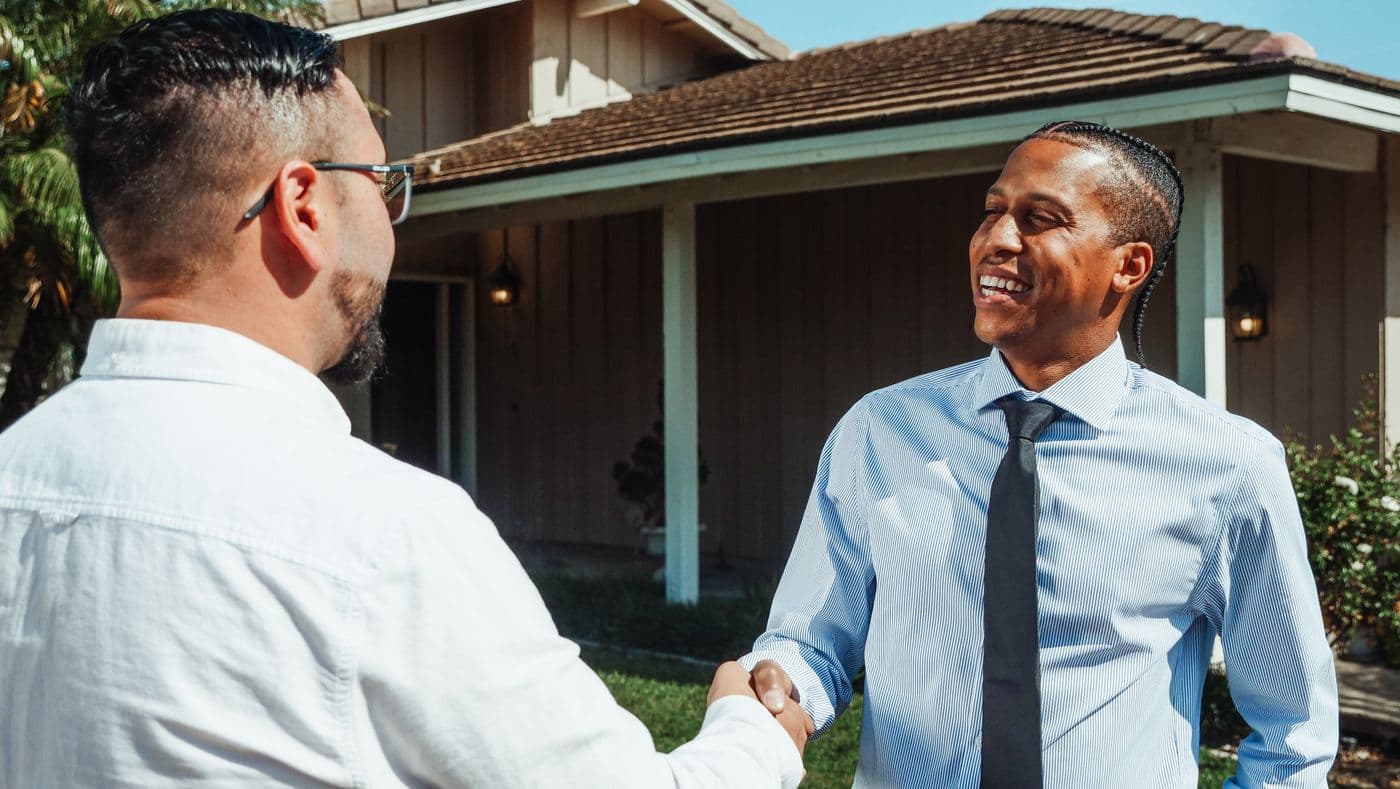 Real estate agent shaking hands with a client in front of a house