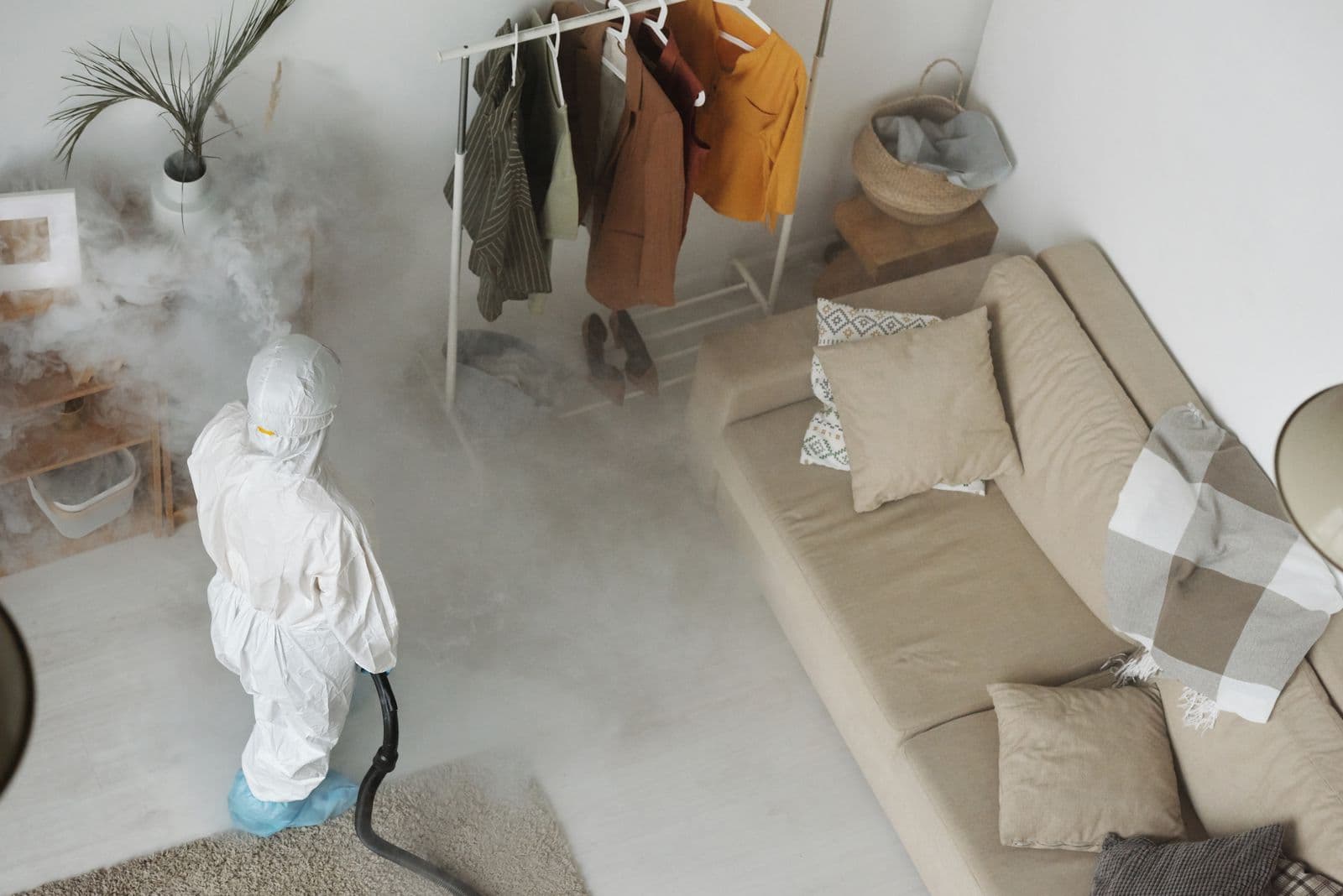 Technician in white protective coveralls fogging a living room with a disinfection sprayer