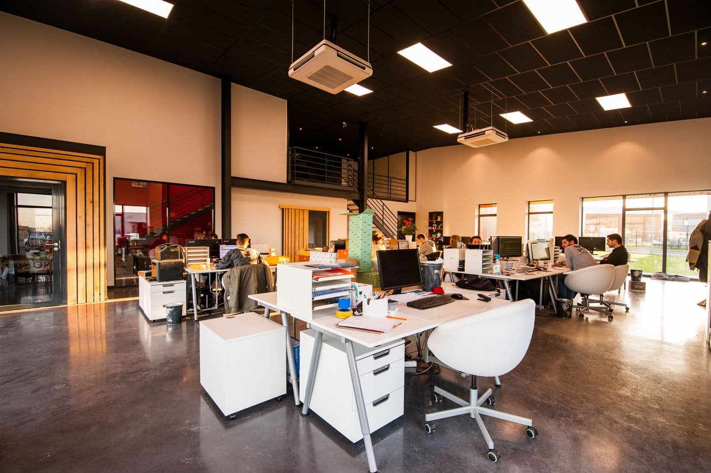 Open-plan office with workstations, ceiling HVAC units, and a mezzanine